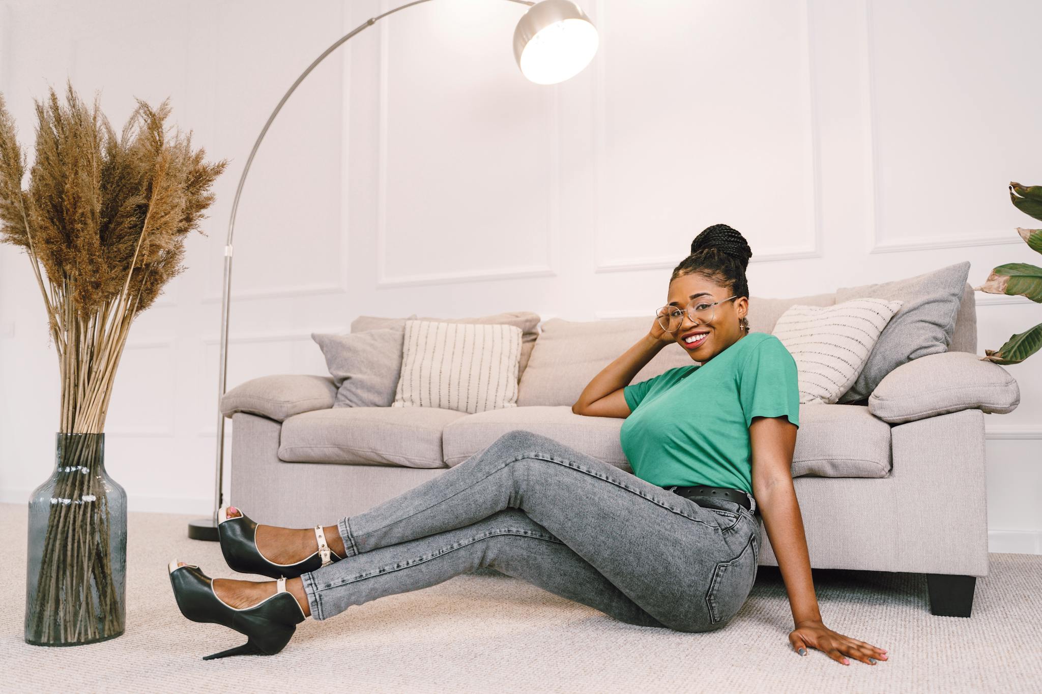A cheerful woman in a stylish outfit poses comfortably in a modern living room, showcasing home decor and fashion.